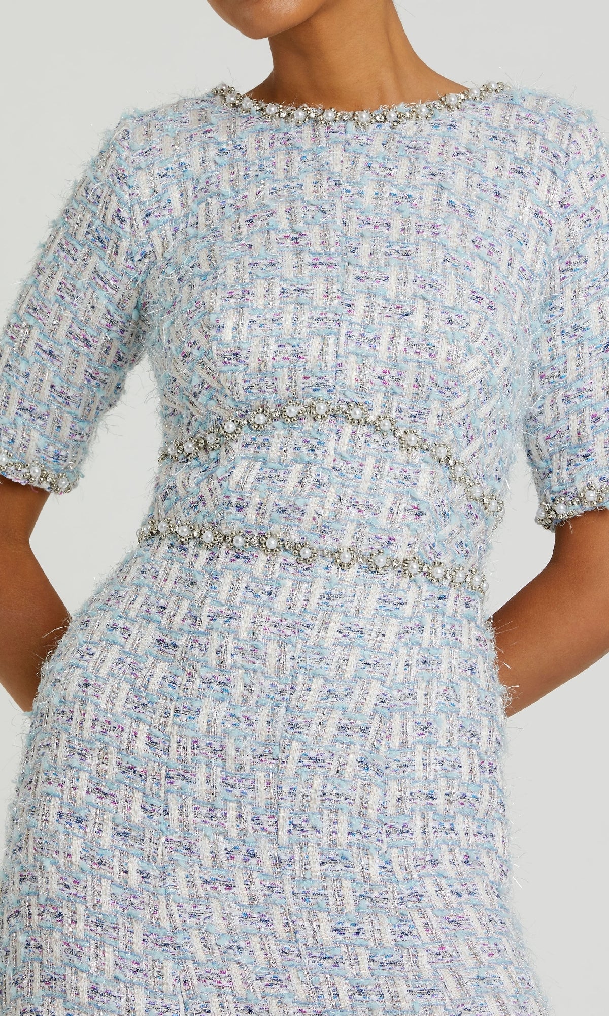 A person wearing the Mac Duggal 20806 Short Blue Wedding Guest Dress, featuring light blue and white tweed, silver embellishments, short sleeves, and a fitted waist.